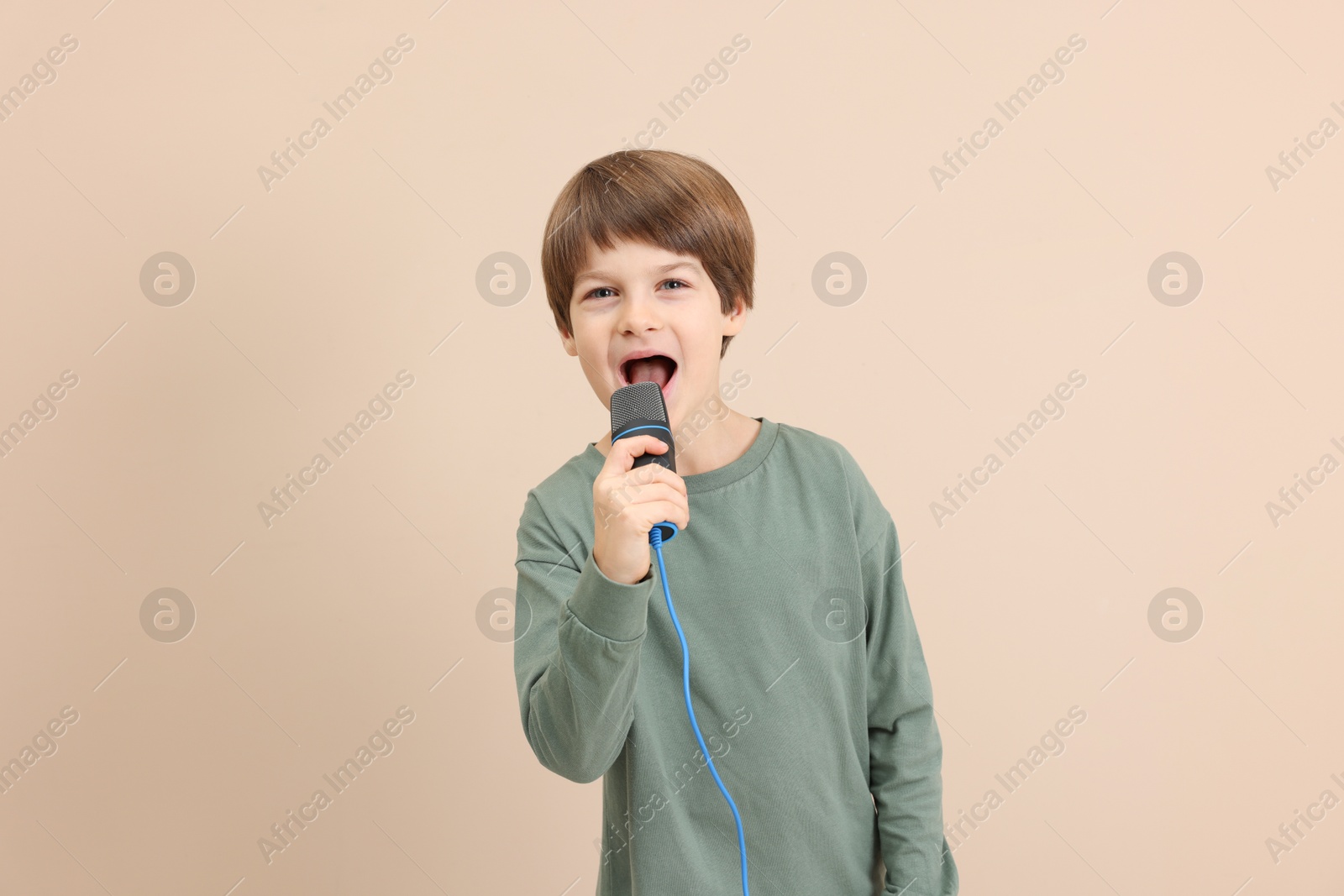 Photo of Cute boy with microphone singing near beige wall