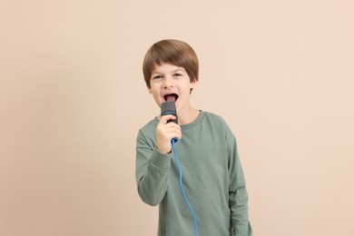 Photo of Cute boy with microphone singing near beige wall