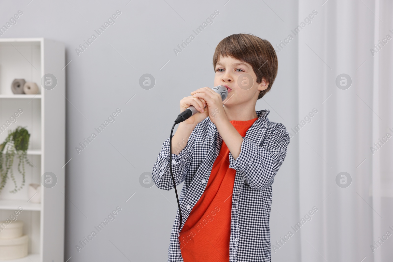 Photo of Cute boy with microphone singing at home. Space for text