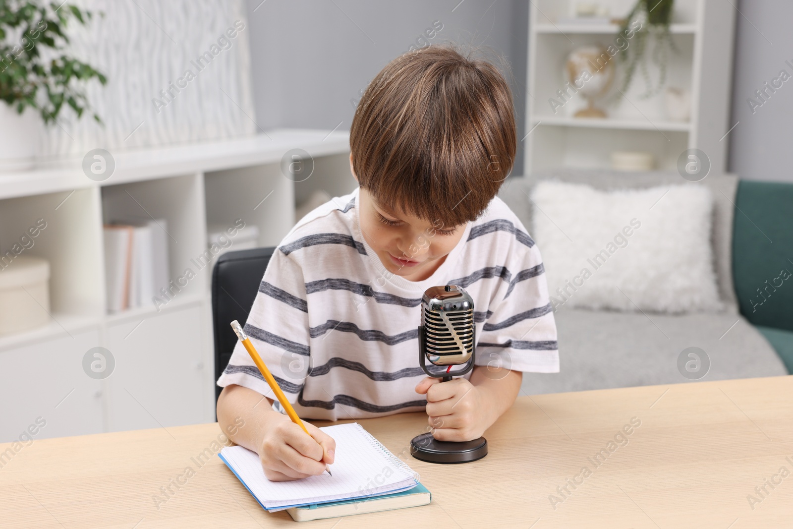 Photo of Cute boy with microphone recording podcast at table indoors