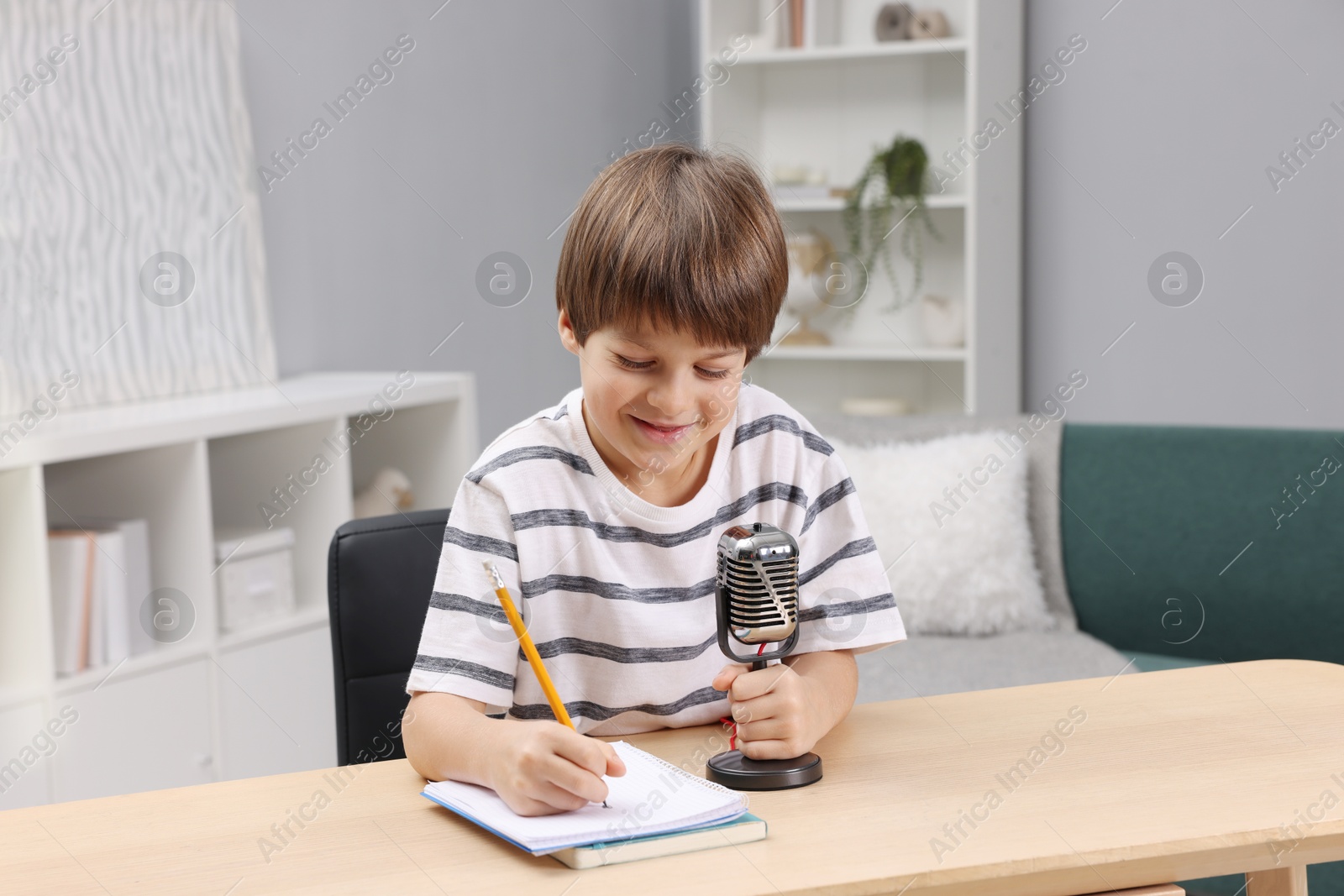 Photo of Cute boy with microphone recording podcast at table indoors