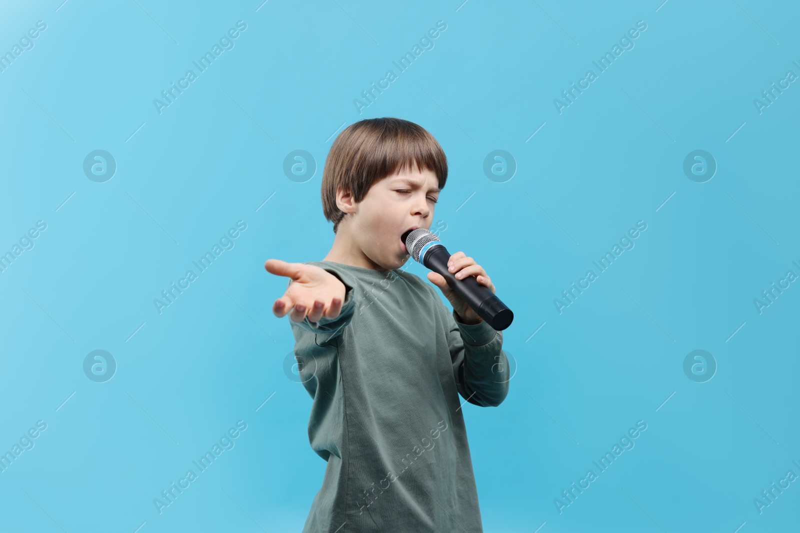 Photo of Cute boy with microphone singing on light blue background