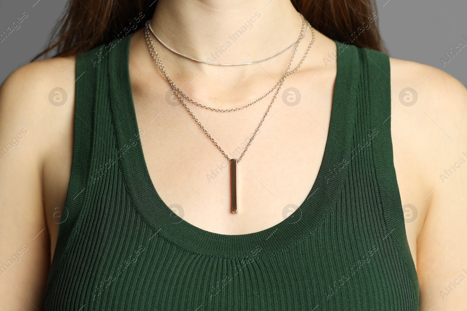 Photo of Woman wearing layered silver necklace on grey background, closeup