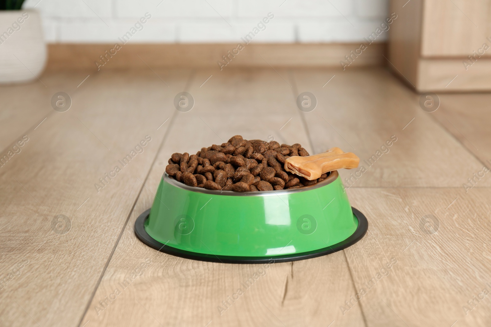 Photo of Dry pet food in feeding bowl and chew bone on floor indoors