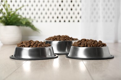 Photo of Dry pet food in feeding bowls on floor indoors