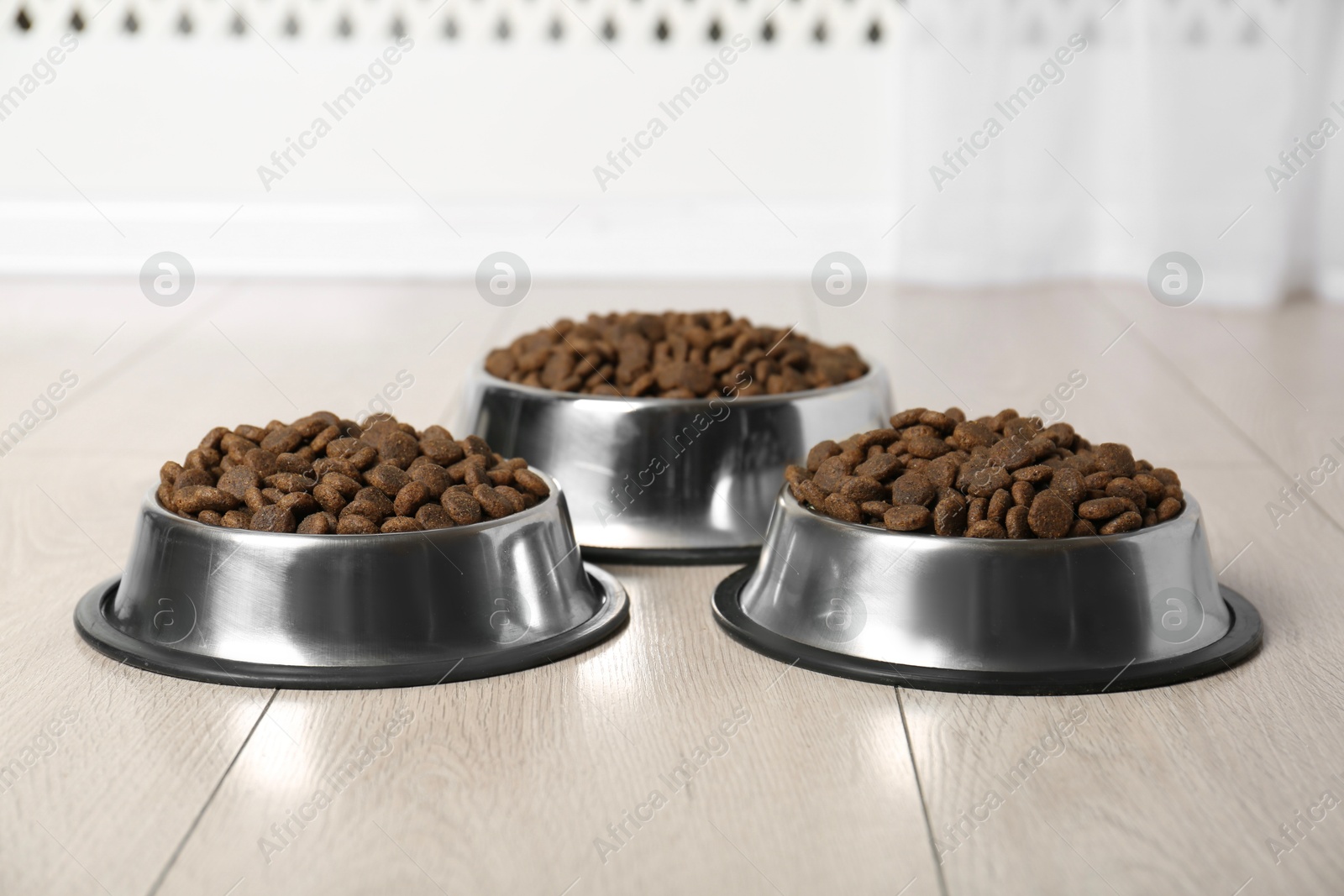 Photo of Dry pet food in feeding bowls on floor indoors