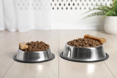 Photo of Dry pet food in feeding bowls and chew bones on floor indoors