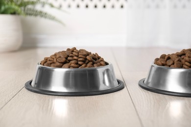 Photo of Dry pet food in feeding bowls on floor indoors