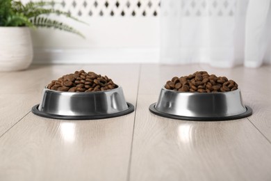 Photo of Dry pet food in feeding bowls on floor indoors