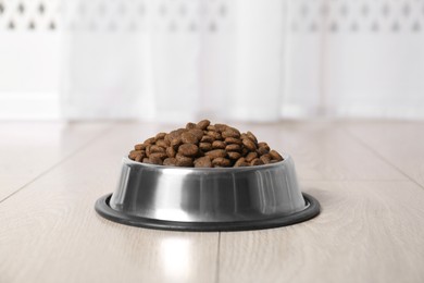 Photo of Dry pet food in feeding bowl on floor indoors