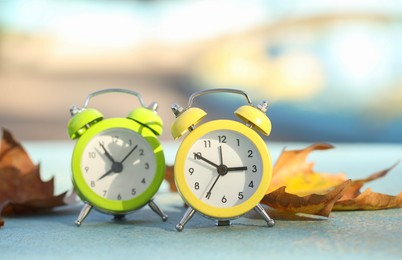 Photo of Autumn time. Alarm clocks and golden leaves on light surface outdoors, closeup