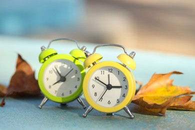 Photo of Autumn time. Alarm clocks and golden leaves on light surface outdoors, closeup