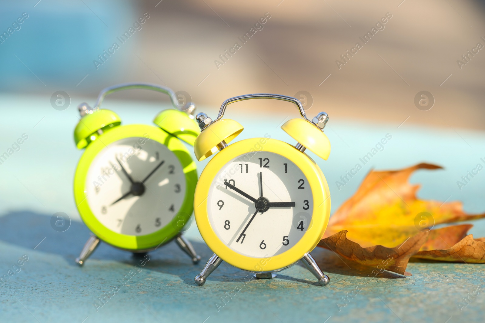 Photo of Autumn time. Alarm clocks and golden leaves on light surface outdoors, closeup