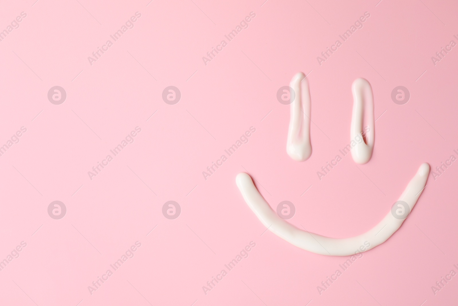 Photo of Smiling face made of cream on pink background, top view. Samples of cosmetic product. Space for text