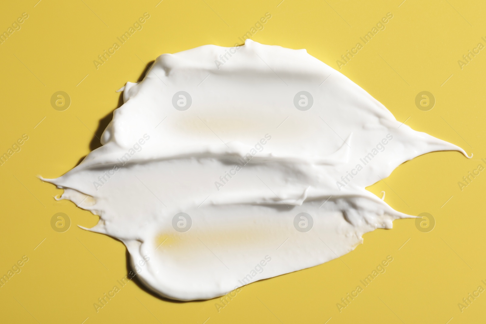 Photo of Cream on yellow background, top view. Sample of cosmetic product