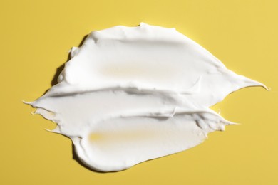 Cream on yellow background, top view. Sample of cosmetic product