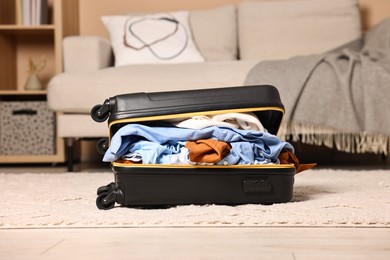 Photo of Open suitcase full of different messy clothes on floor indoors