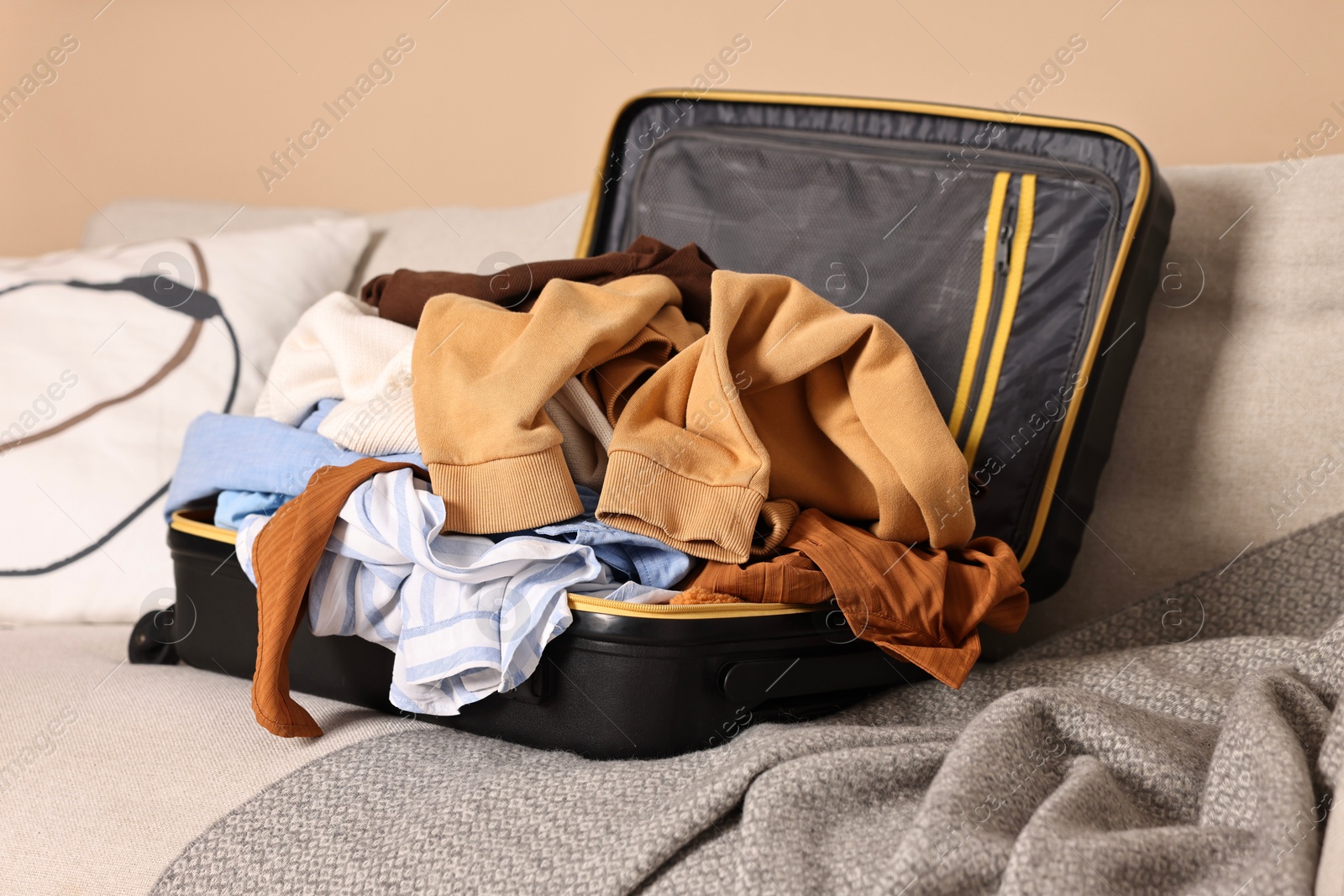 Open suitcase full of different messy clothes on sofa indoors Photo of Open suitcase full of different messy clothes on sofa indoors