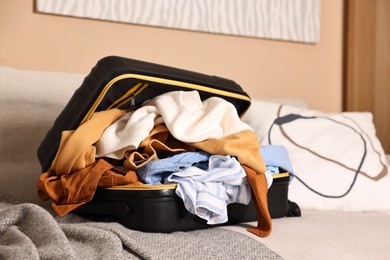 Photo of Open suitcase full of different messy clothes on sofa indoors