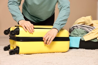 Photo of Woman closing suitcase near pile of different messy clothes indoors, closeup