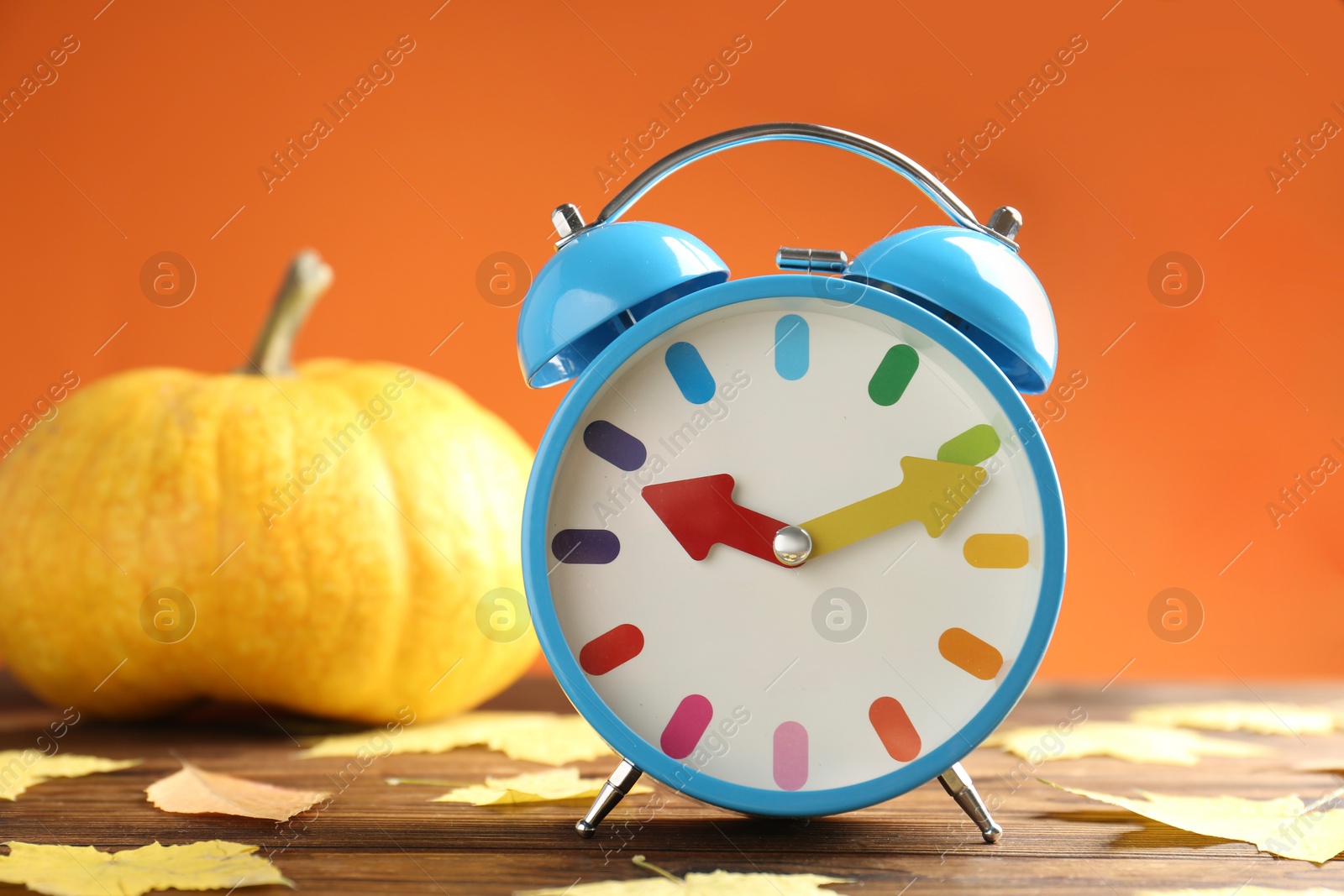 Photo of Autumn time. Alarm clock and golden leaves on wooden table