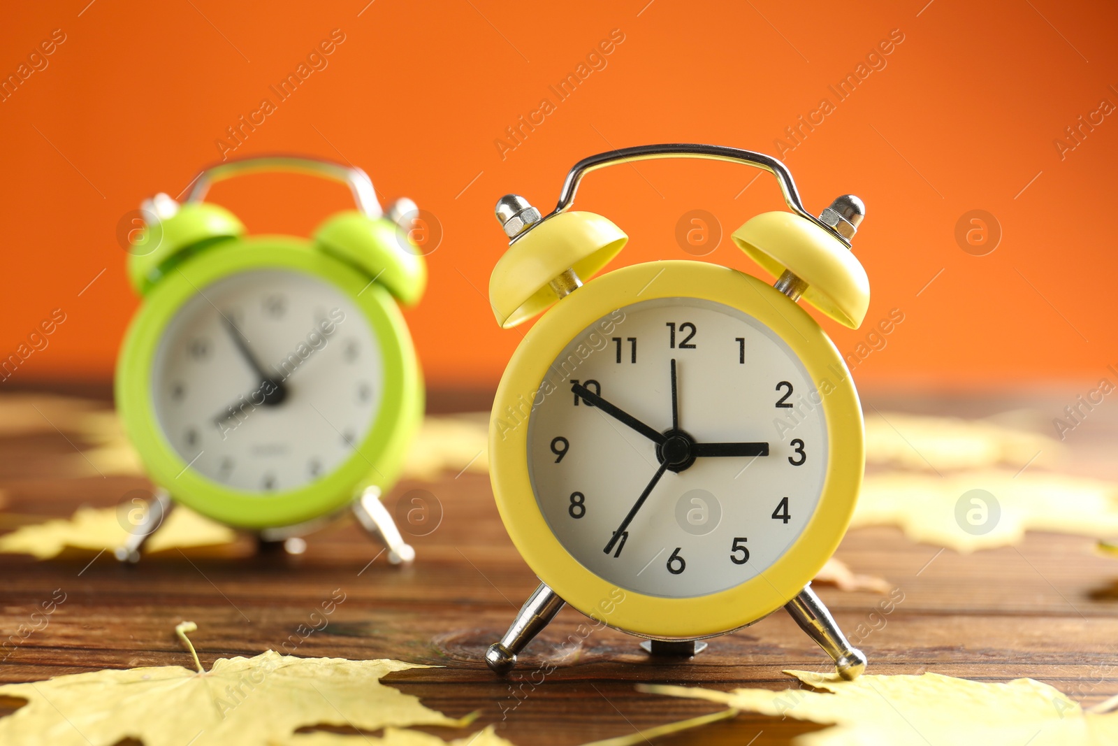 Photo of Autumn time. Alarm clocks and golden leaves on wooden table, selective focus