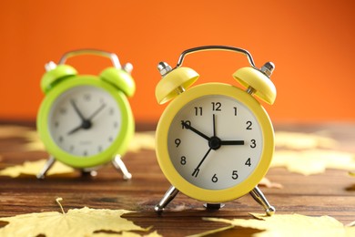 Photo of Autumn time. Alarm clocks and golden leaves on wooden table, selective focus