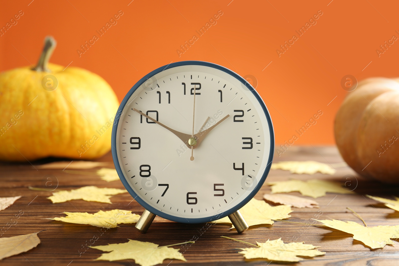 Photo of Autumn time. Alarm clock and golden leaves on wooden table