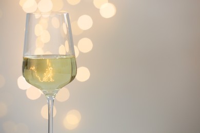 Photo of Tasty white wine in glass against grey background with blurred lights, closeup. Bokeh effect