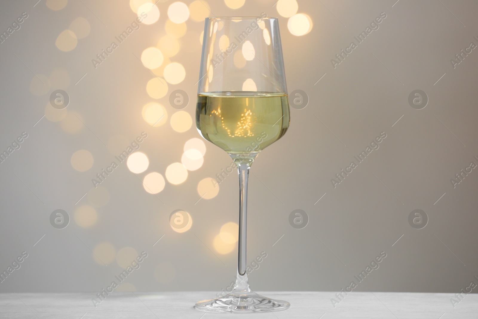 Photo of Tasty white wine in glass on table against grey background with blurred lights, bokeh effect