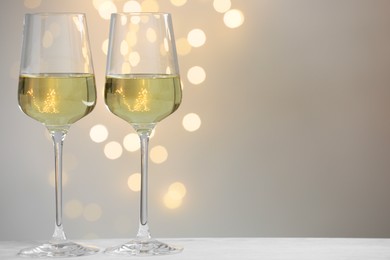 Photo of Tasty white wine in glasses on table against grey background with blurred lights, bokeh effect. Space for text