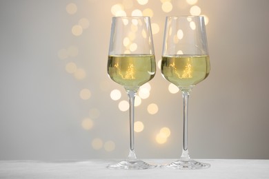 Photo of Tasty white wine in glasses on table against grey background with blurred lights, bokeh effect. Space for text