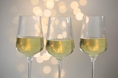 Tasty white wine in glasses against grey background with blurred lights, closeup. Bokeh effect