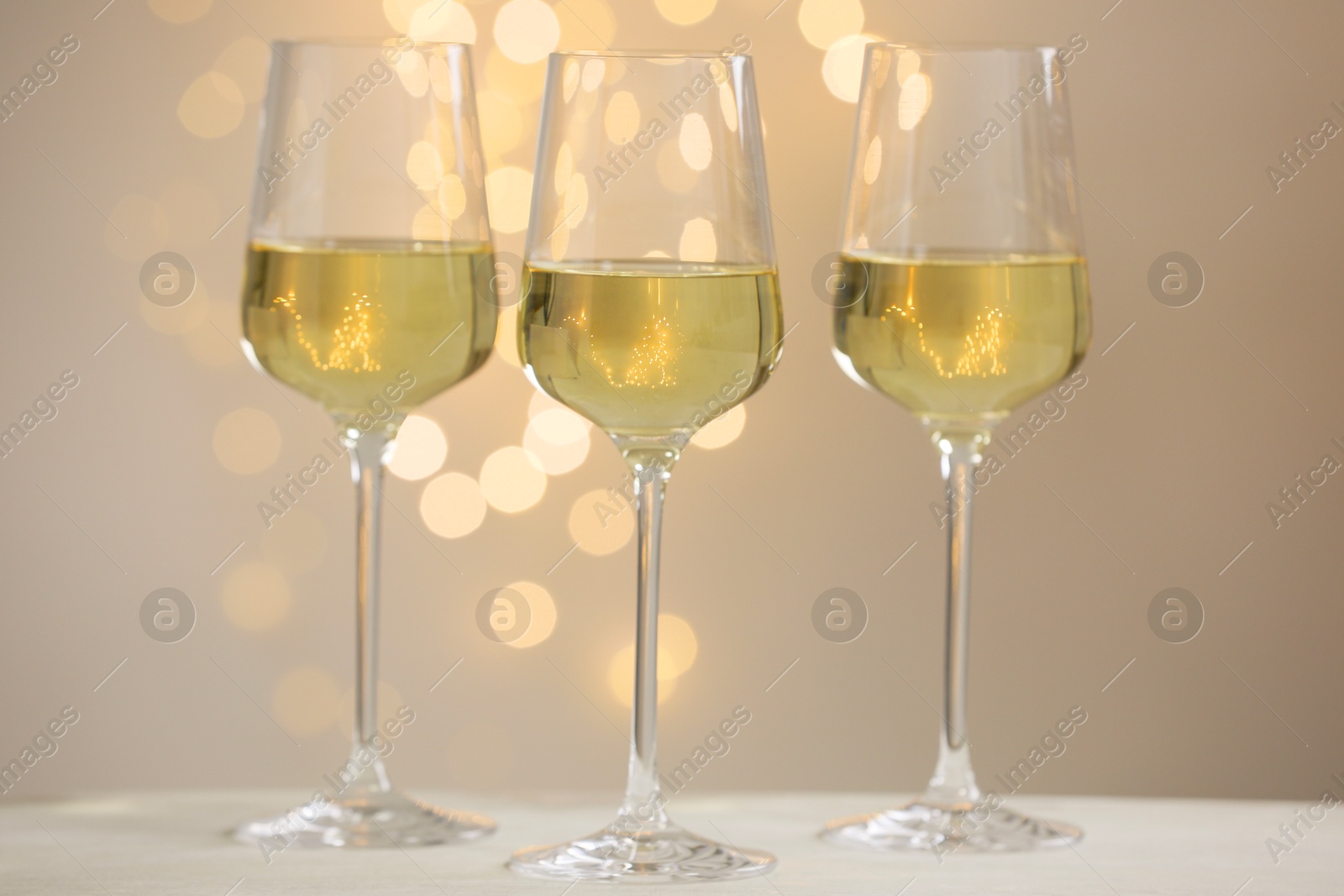 Tasty white wine in glasses on table against grey background with blurred lights, bokeh effect Photo of Tasty white wine in glasses on table against grey background with blurred lights, bokeh effect