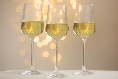 Photo of Tasty white wine in glasses on table against grey background with blurred lights, bokeh effect