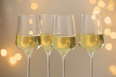 Photo of Tasty white wine in glasses against grey background with blurred lights, closeup. Bokeh effect