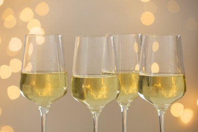 Photo of Tasty white wine in glasses against grey background with blurred lights, closeup. Bokeh effect