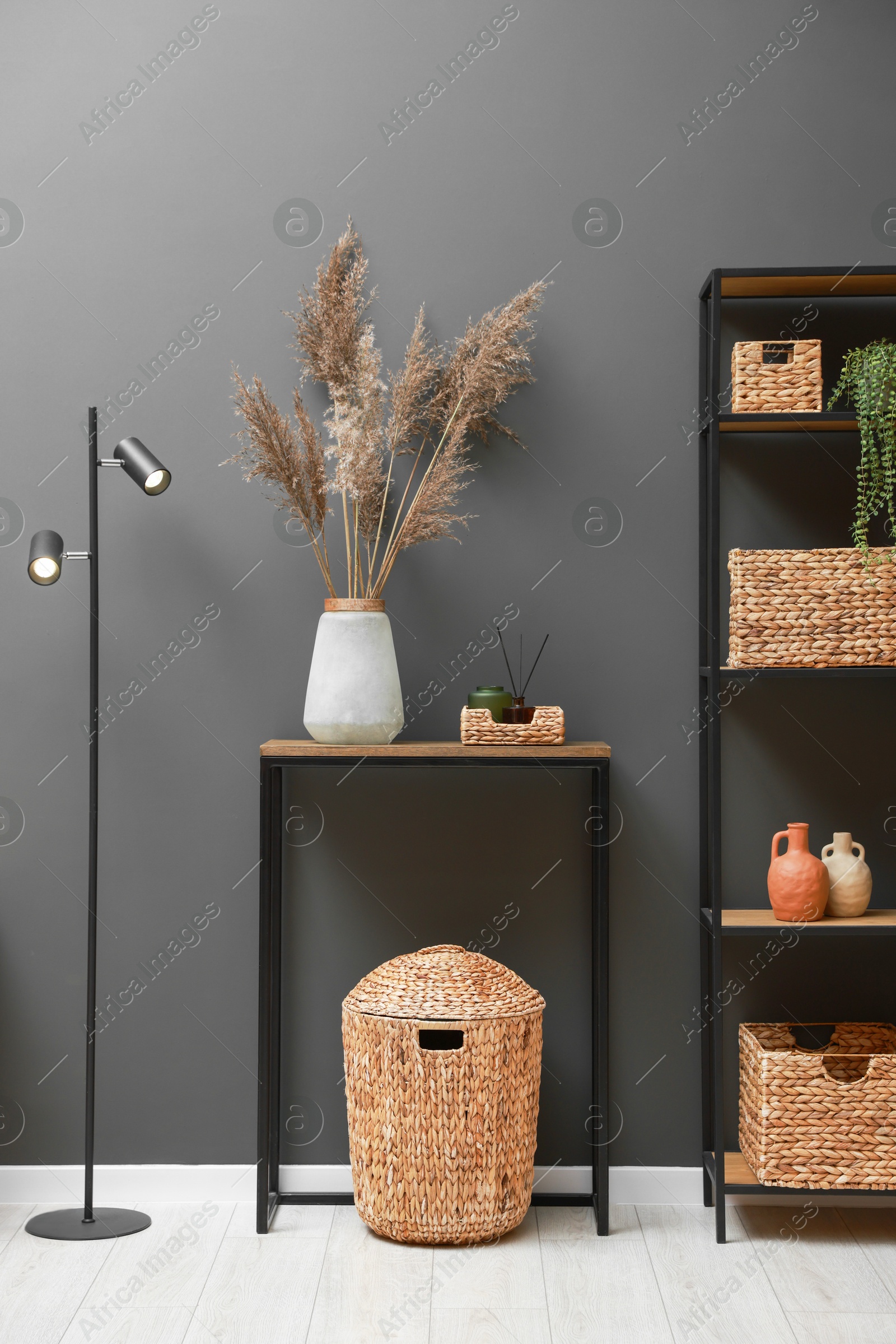 Photo of Console table with decor, lamp and shelving unit near grey wall in room. Interior design