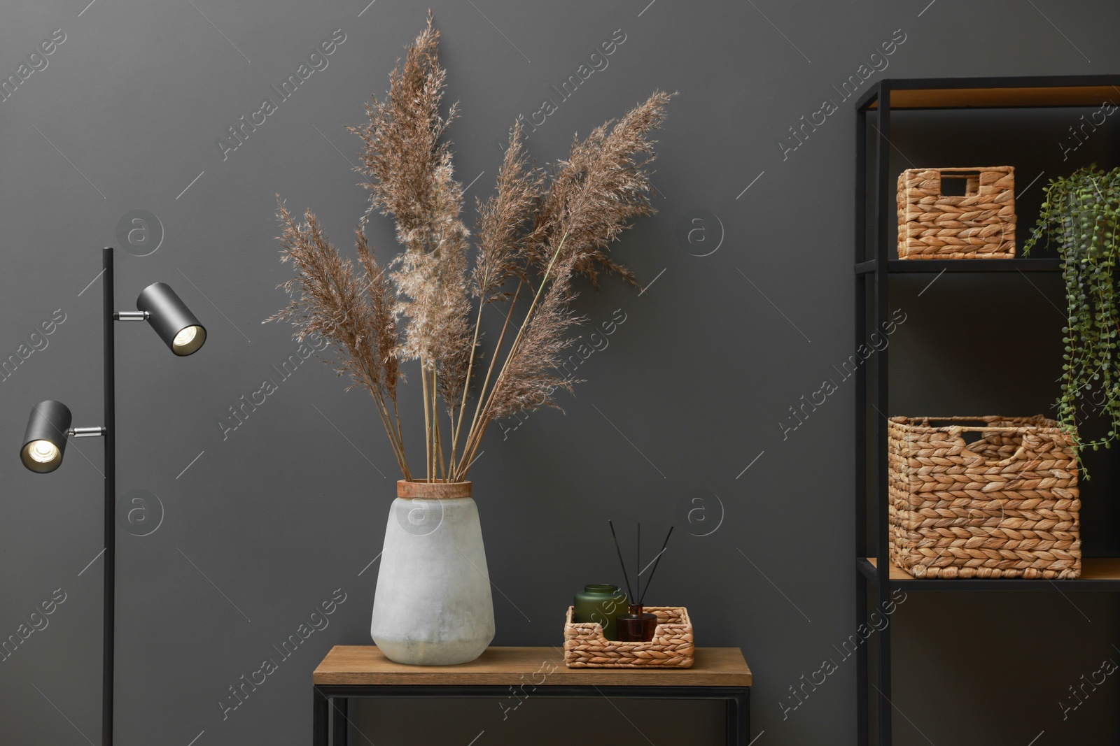 Photo of Console table with decor, lamp and shelving unit near grey wall in room. Interior design