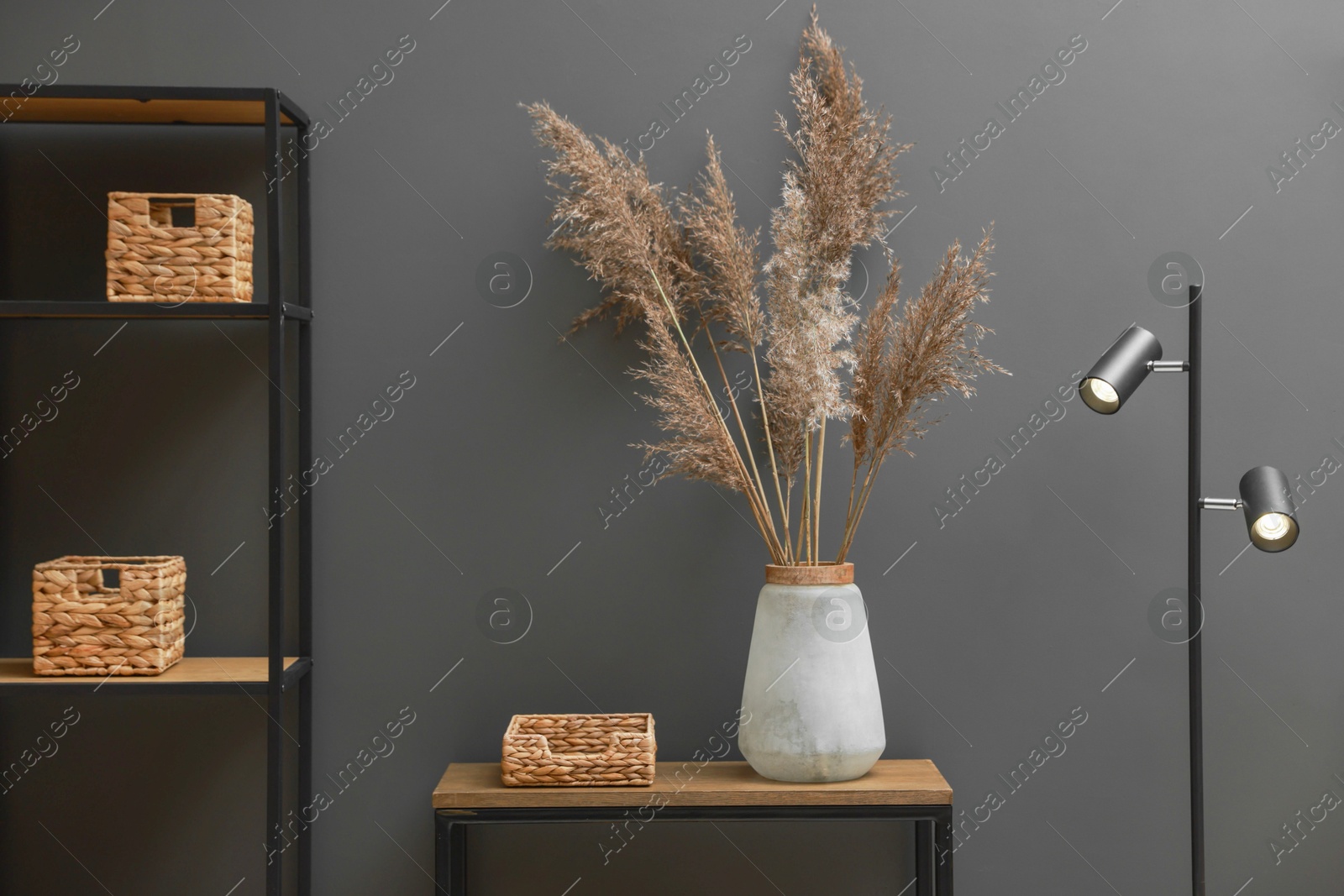 Photo of Console table with decor, lamp and shelving unit near grey wall in room. Interior design