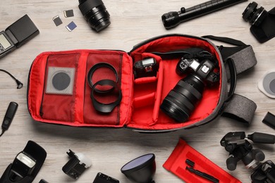 Professional photographer's equipment and backpack on light wooden background, flat lay