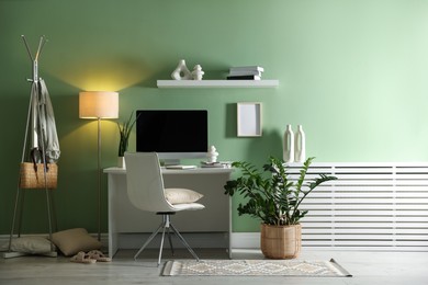 Photo of Home office. Comfortable workplace with desk, computer and lamp near light green wall in room