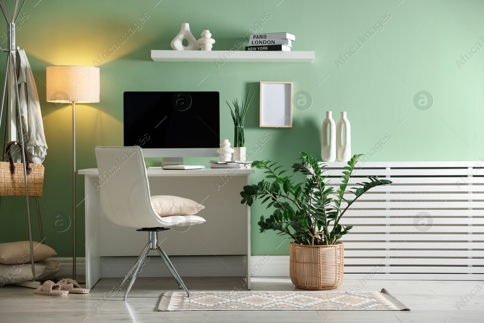 Photo of Home office. Comfortable workplace with desk, computer and lamp near light green wall in room