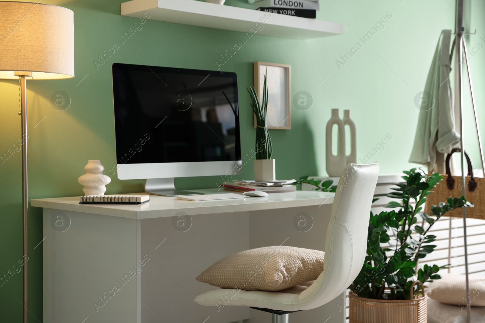 Photo of Home office. Comfortable workplace with desk, computer and lamp near light green wall in room