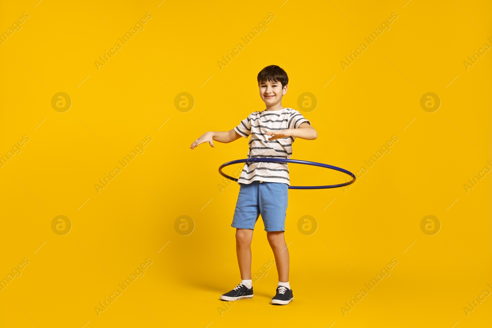 Photo of Smiling boy exercising with hula hoop on yellow background, space for text