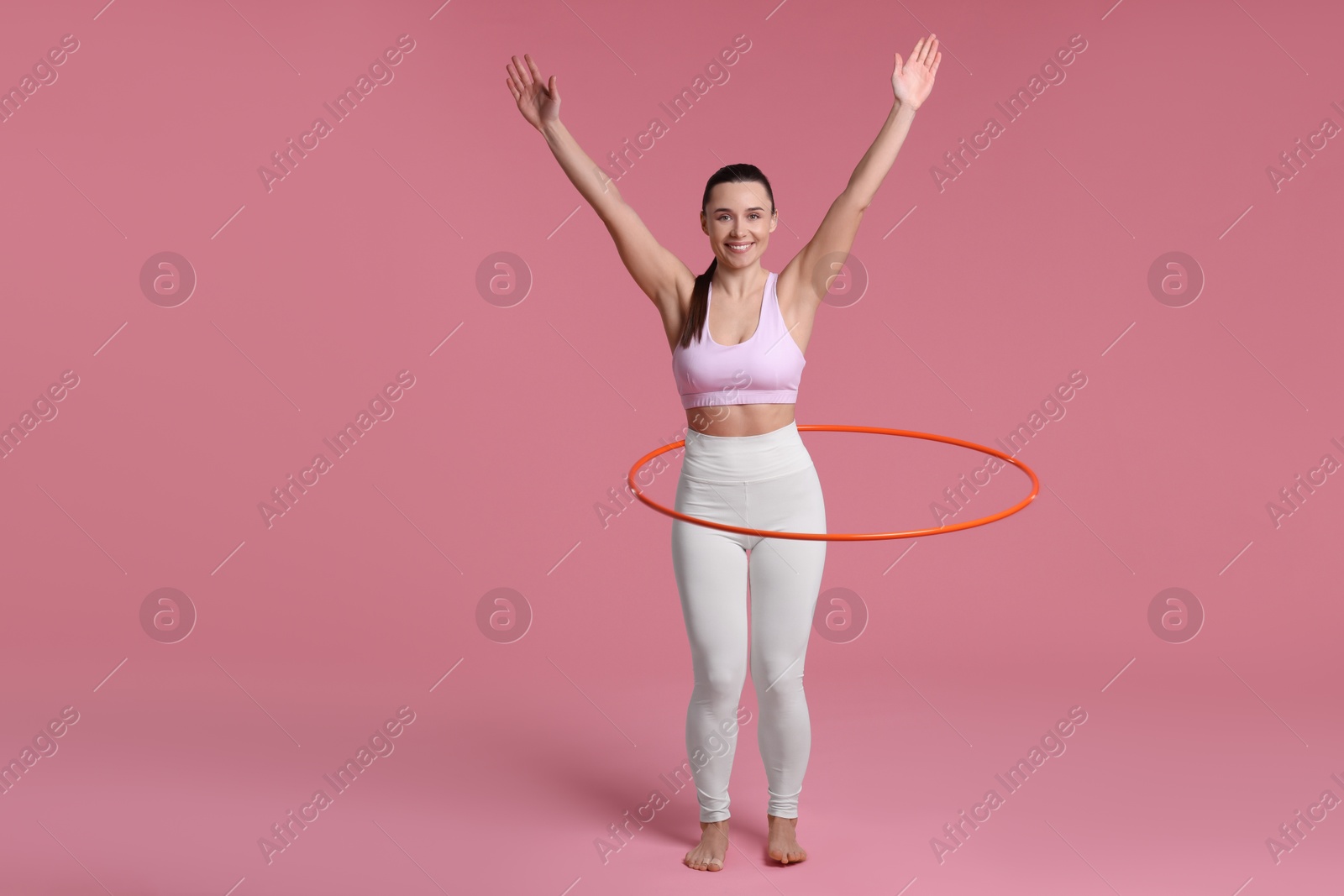 Photo of Smiling woman training with hula hoop on pink background