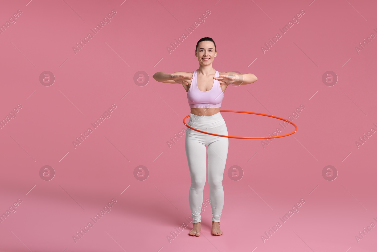 Photo of Smiling woman training with hula hoop on pink background