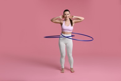 Photo of Smiling woman training with hula hoops on pink background