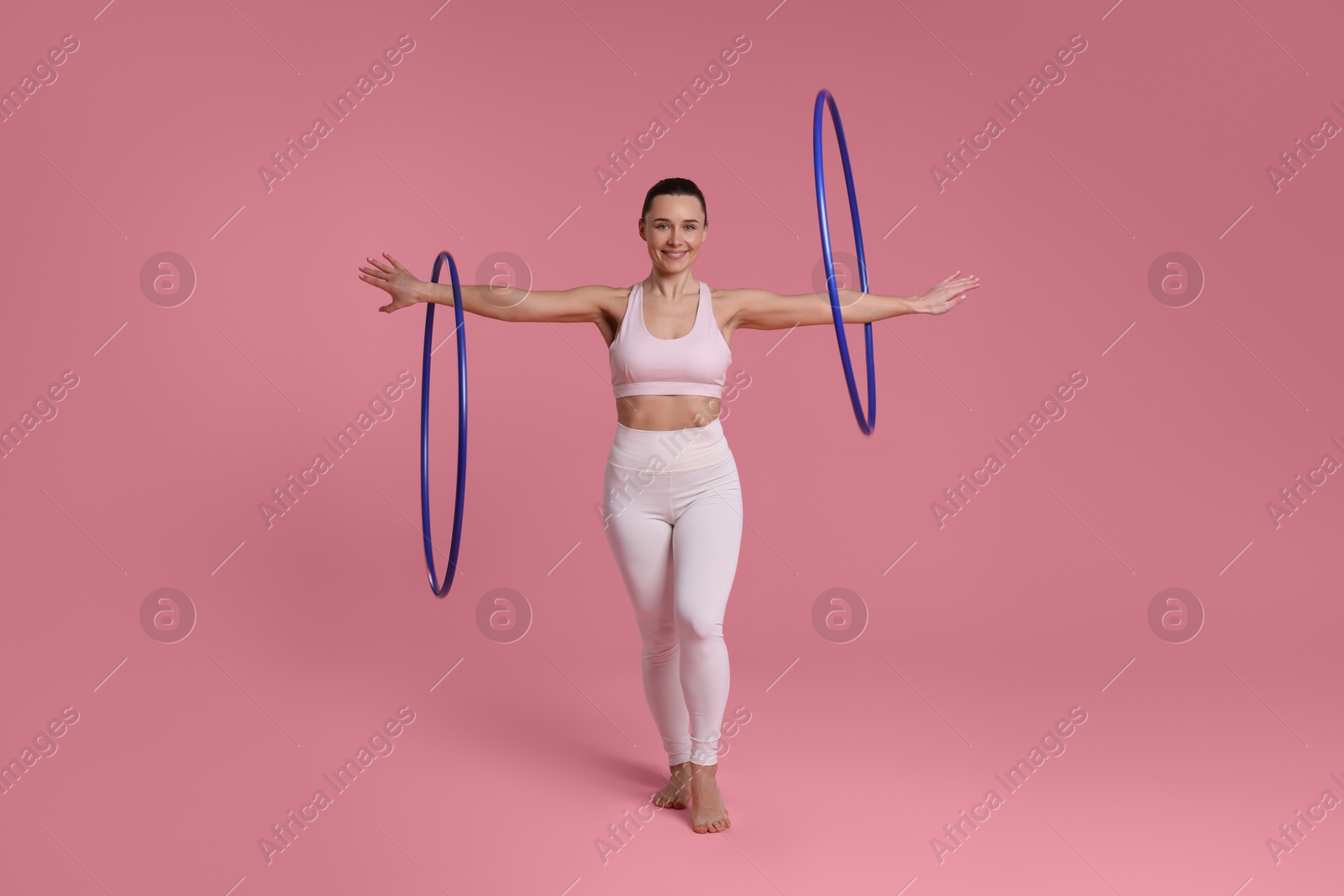 Photo of Smiling woman training with hula hoops on pink background