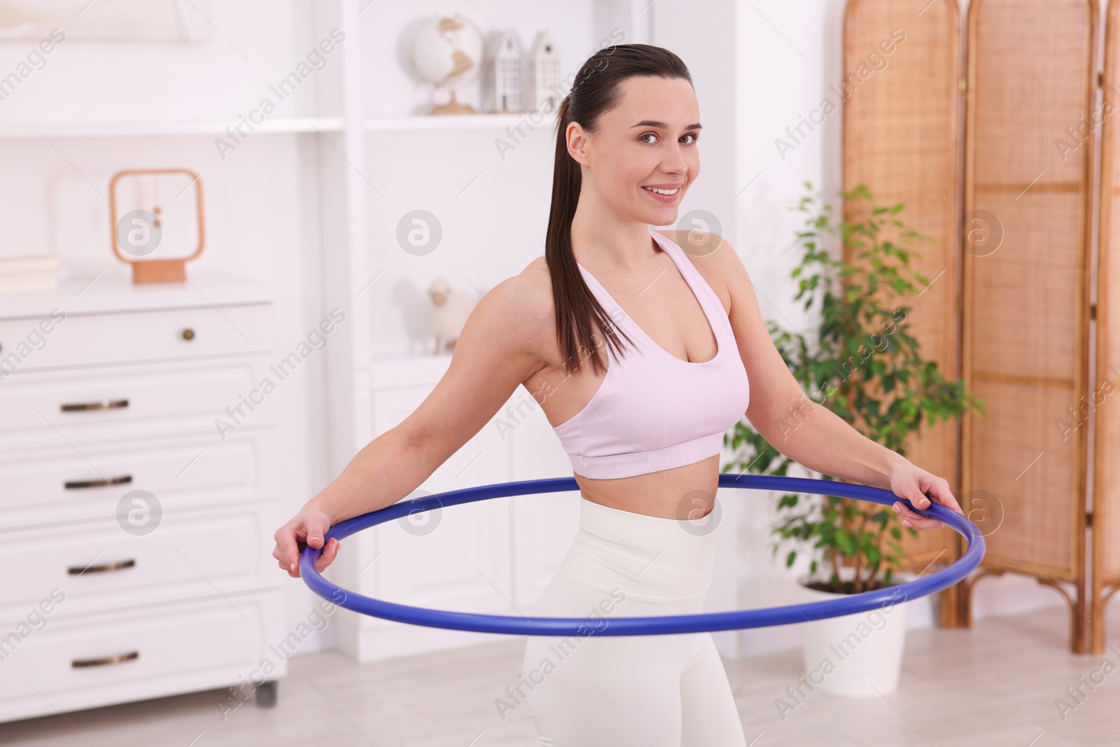 Photo of Smiling woman training with hula hoop at home